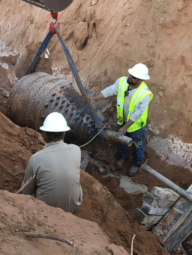 Crew in hard hats lowering large-diameter pipe into an excavation